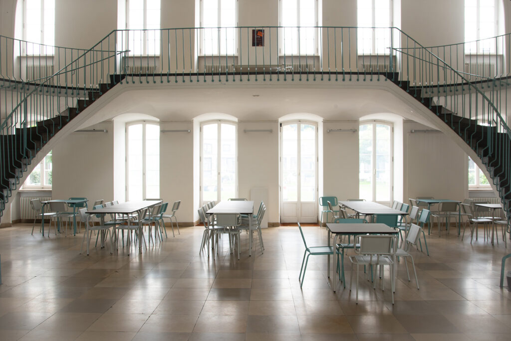 Heller Veranstaltungsraum mit Tischen und Stühlen, große Fenster, elegante Architektur.