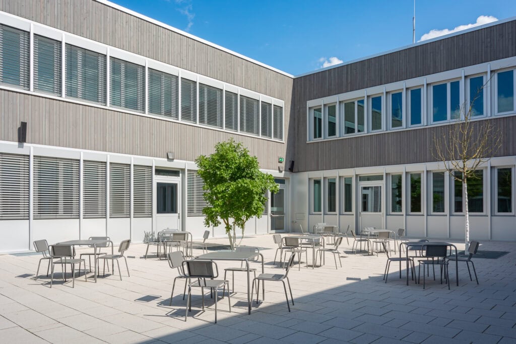 Moderne Schulhof mit Stahlmöbeln und Bäumen im Innenhof.