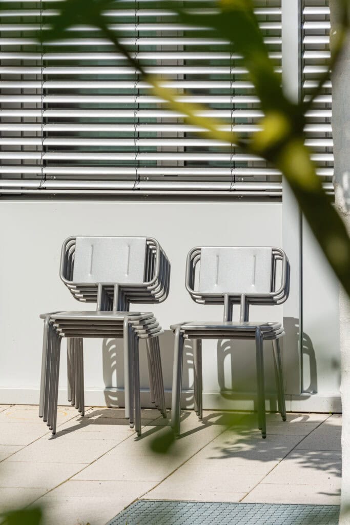 Zwei moderne Stahlstühle vor Fenster mit Jalousien, minimalistisch und robust.