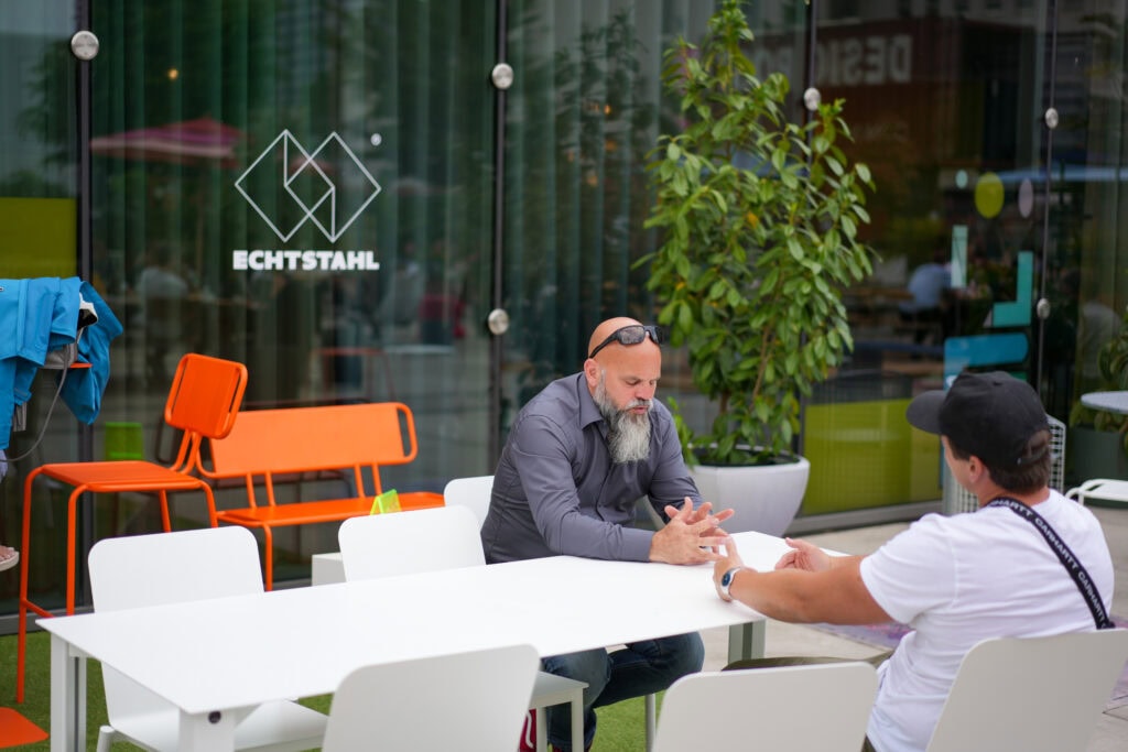 Zwei Männer im Gespräch vor einem Echtstahl-Stahlmöbelgeschäft in Köln.